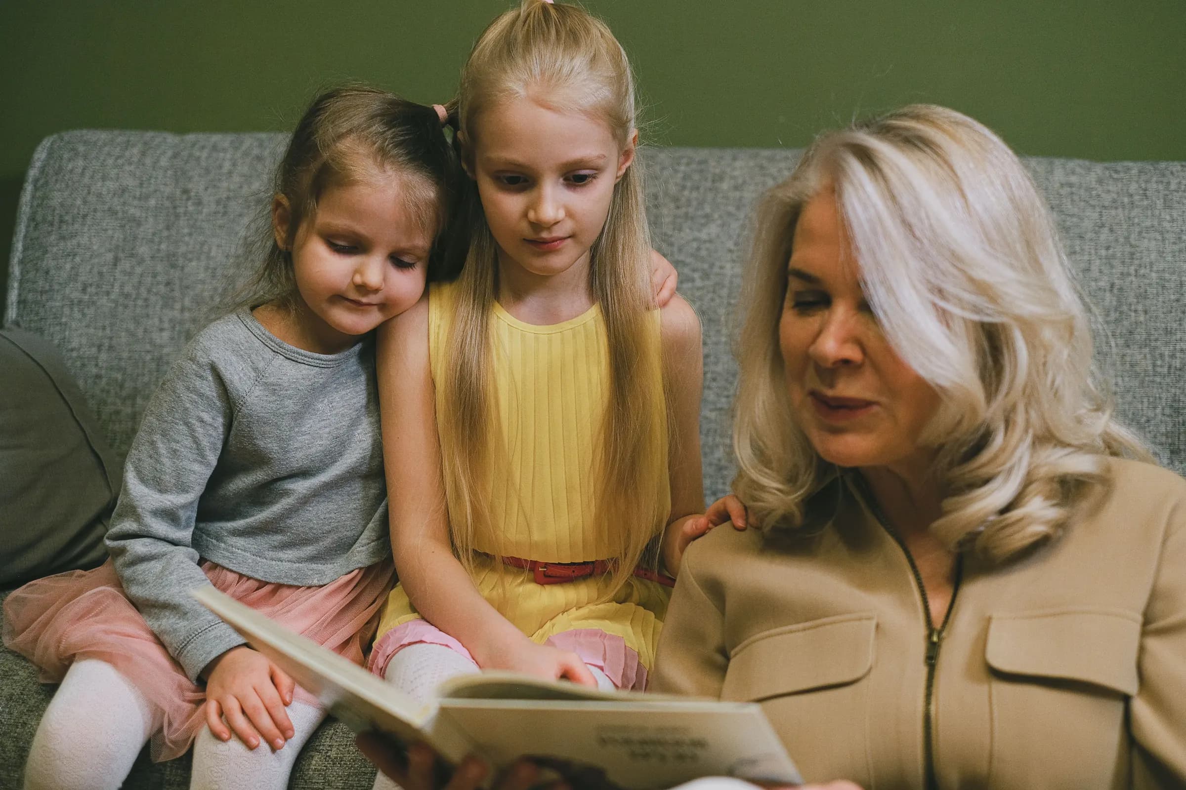 Oma liest ihren zwei Enkelinnen auf dem Sofa aus einem Buch vor.