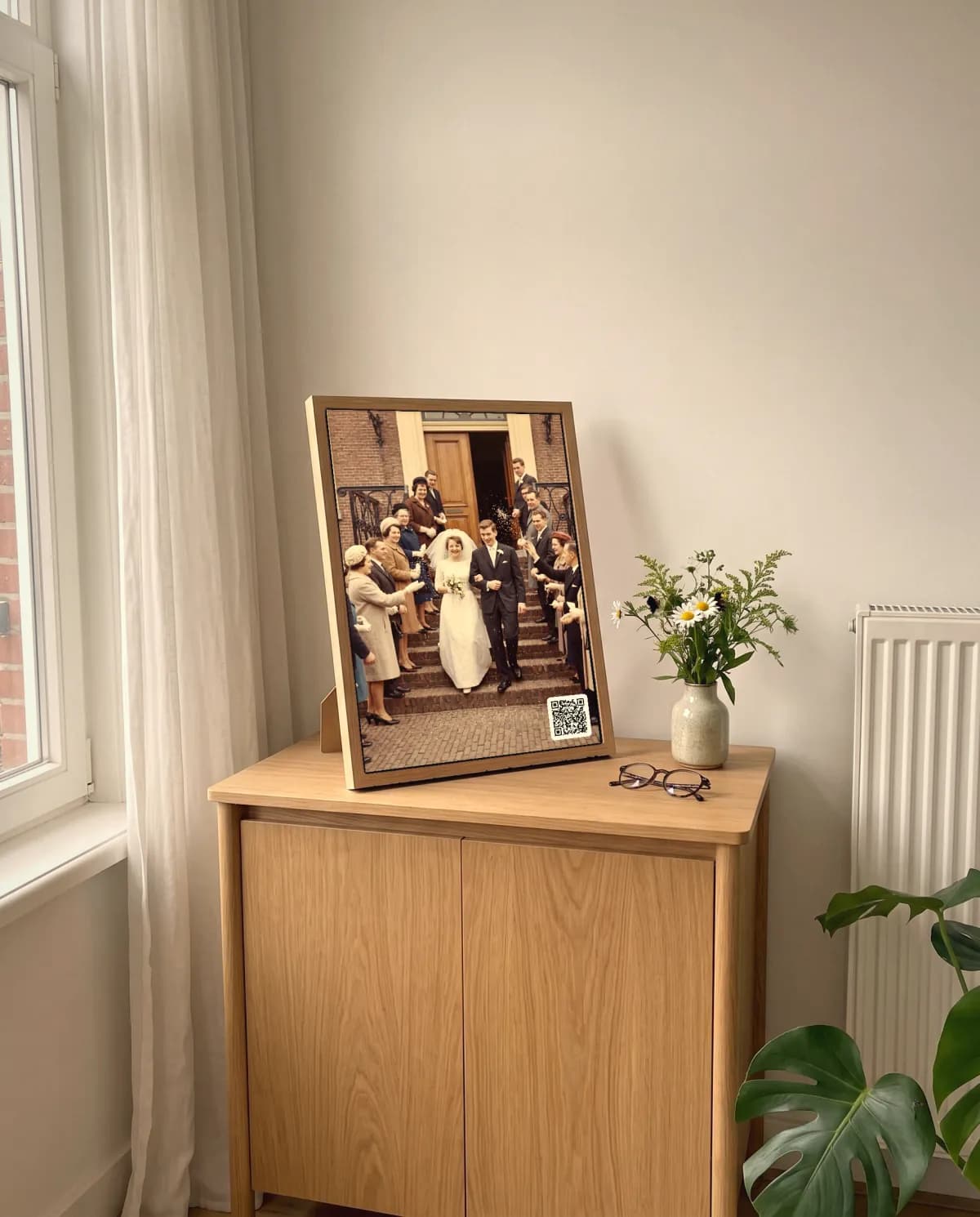 Ein Geschichtenrahmen mit einem Hochzeitsfoto von 1962 und einem QR-Code in der Ecke, auf einem Eichenschrank in einem hellen Wohnzimmer